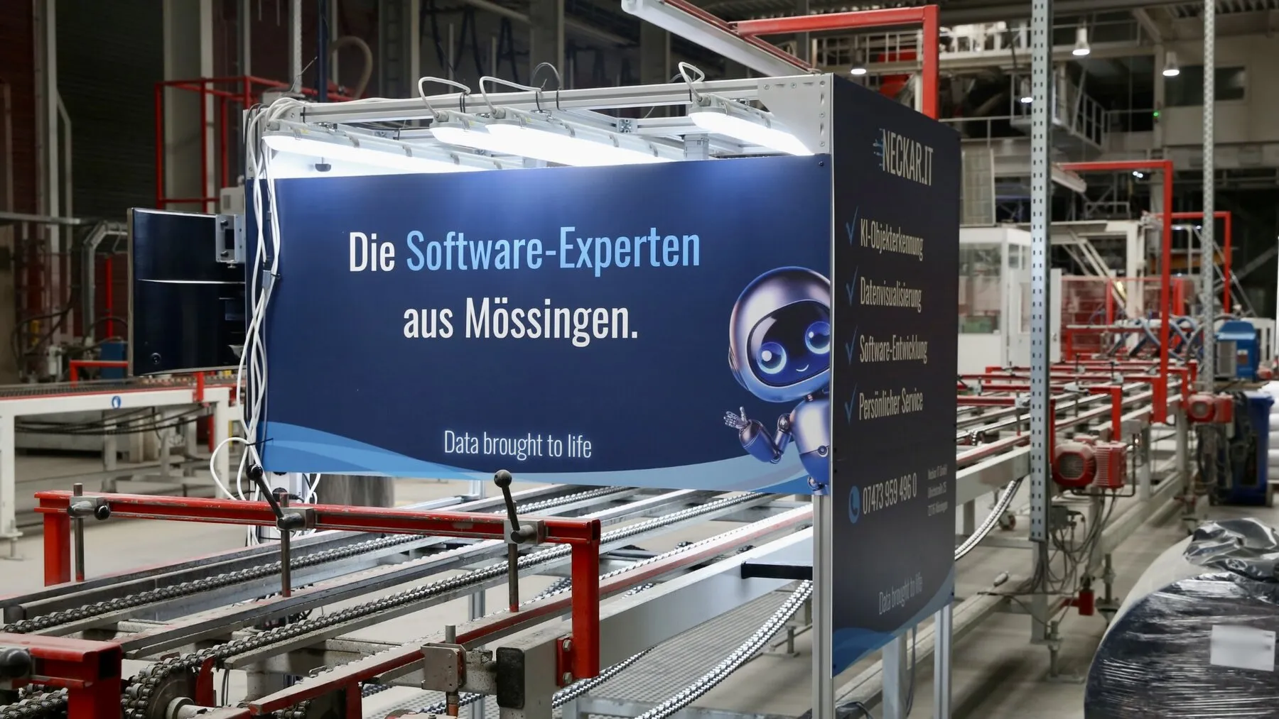 Prüfaufbau der KI-Qualitätskontrolle über der Produktionslinie: Kameras und LED-Beleuchtung am Rahmen, verkleidet im Neckar-IT-Branding